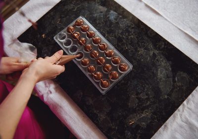 Top view of a chocolatier holding a candy bag and squeezing liquid warm chocolate mass into candy molds. Process making handmade luxurious chocolates.